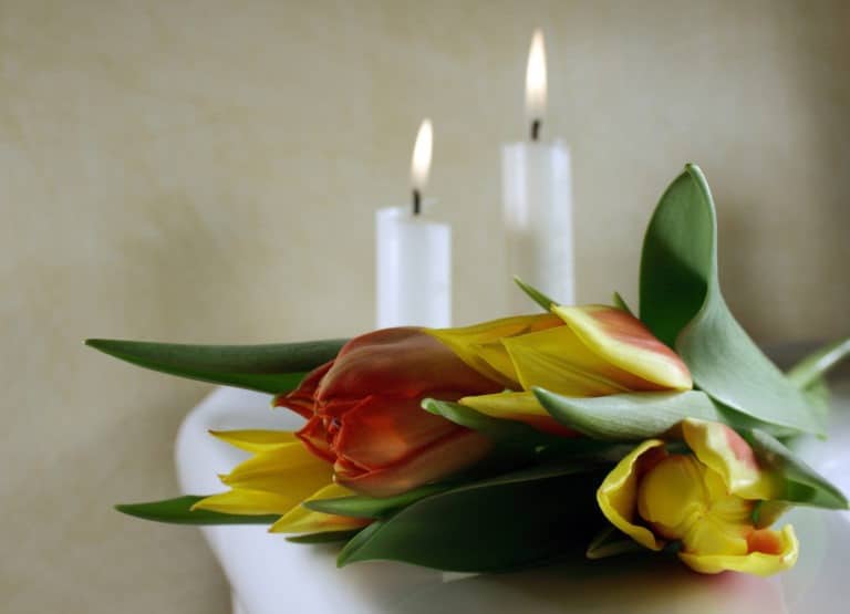 A burning candle with a white coffin and a flower arrangement on the background in a mortuary